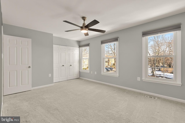 unfurnished bedroom featuring ceiling fan, multiple windows, a closet, and light carpet