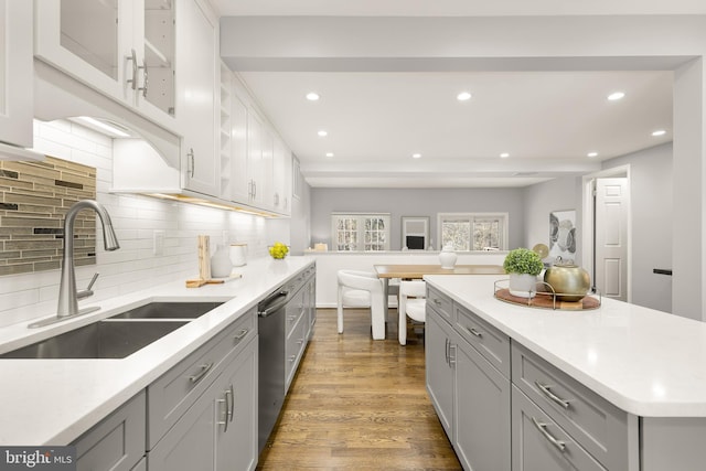 kitchen featuring hardwood / wood-style floors, decorative backsplash, sink, gray cabinets, and stainless steel dishwasher