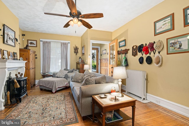 living room featuring ceiling fan, light hardwood / wood-style floors, radiator heating unit, and a textured ceiling