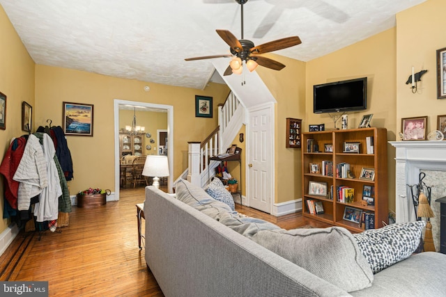 living room with a textured ceiling, a premium fireplace, light hardwood / wood-style flooring, and ceiling fan with notable chandelier