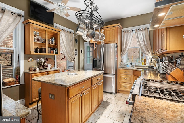 kitchen featuring a center island, sink, ceiling fan, light stone countertops, and stainless steel fridge with ice dispenser