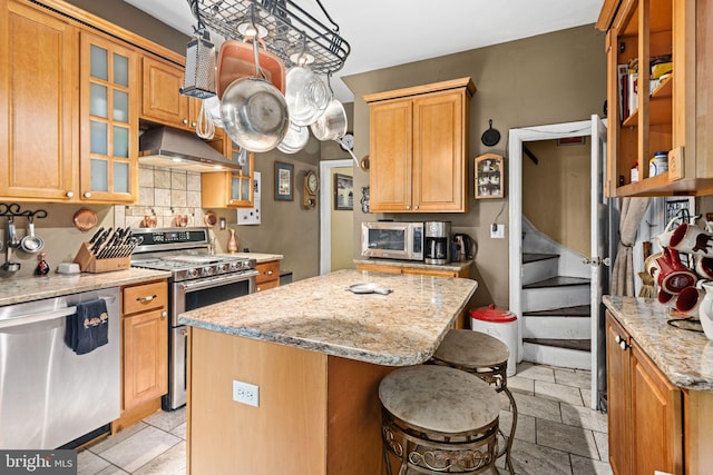 kitchen with a breakfast bar, a center island, ventilation hood, appliances with stainless steel finishes, and light stone counters