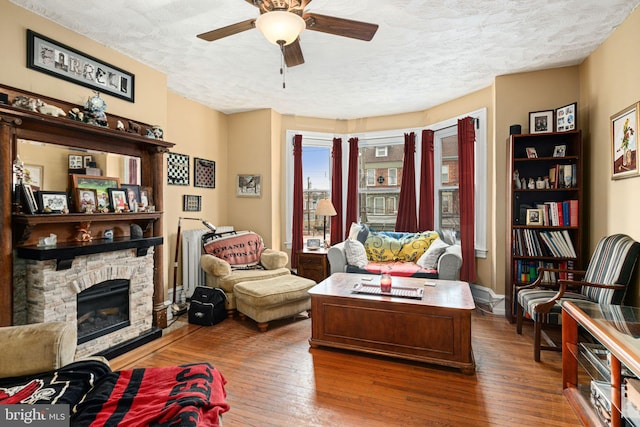 living room featuring a stone fireplace, ceiling fan, wood-type flooring, and a textured ceiling