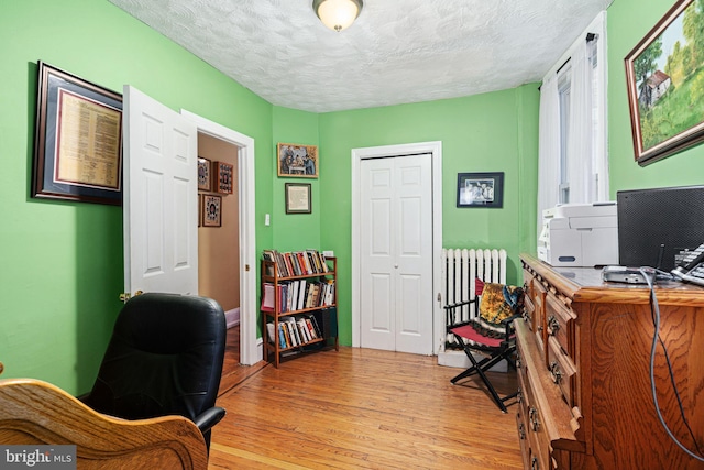 office featuring radiator, light hardwood / wood-style floors, and a textured ceiling