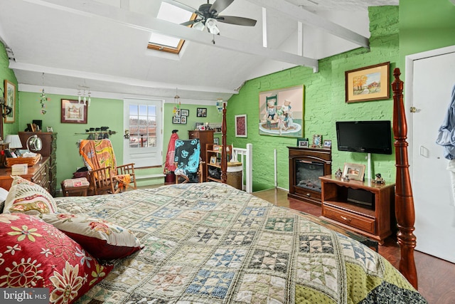 bedroom featuring ceiling fan, brick wall, hardwood / wood-style floors, a fireplace, and vaulted ceiling with skylight