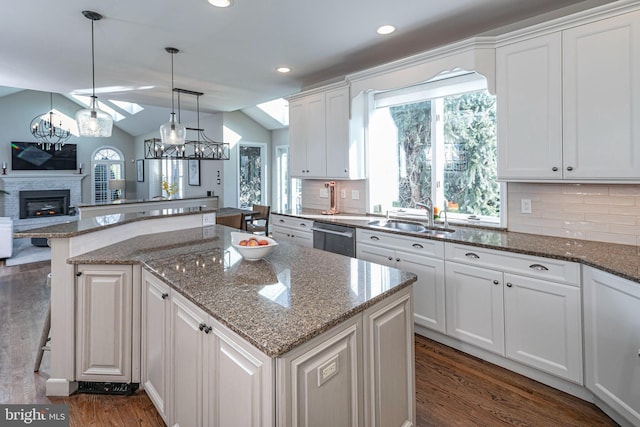 kitchen featuring a breakfast bar, sink, a fireplace, white cabinetry, and lofted ceiling