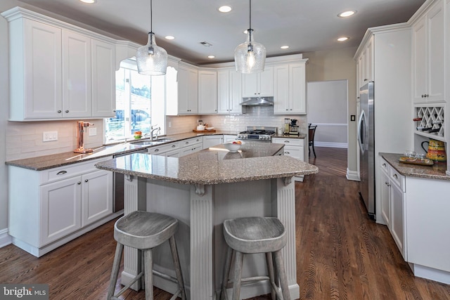 kitchen featuring pendant lighting, dark wood-type flooring, white cabinets, a kitchen island, and a kitchen bar