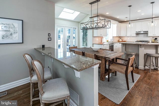 kitchen with white cabinets, light stone countertops, hanging light fixtures, and a breakfast bar area