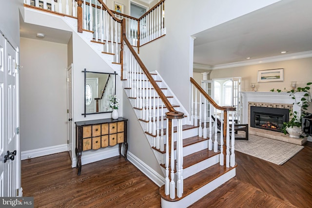 stairway featuring hardwood / wood-style floors, crown molding, and a tile fireplace