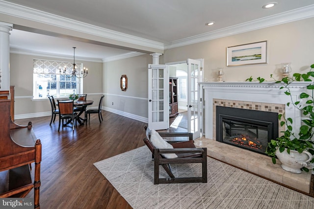 living room featuring ornate columns, dark wood-type flooring, crown molding, a notable chandelier, and a fireplace