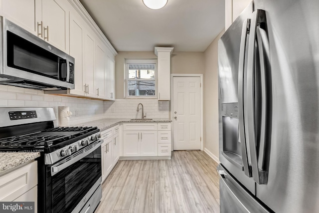 kitchen featuring appliances with stainless steel finishes, light wood-type flooring, light stone counters, sink, and white cabinetry