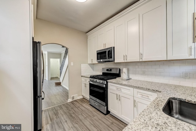 kitchen featuring white cabinets, light stone counters, light wood-type flooring, and stainless steel appliances