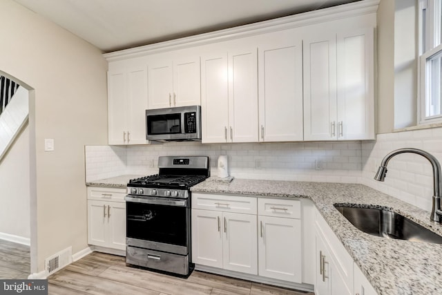 kitchen featuring appliances with stainless steel finishes, light stone counters, white cabinetry, and sink