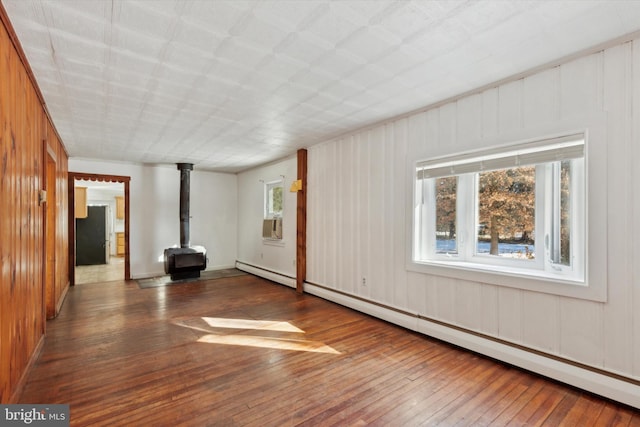 spare room featuring baseboard heating, a wood stove, and dark hardwood / wood-style floors