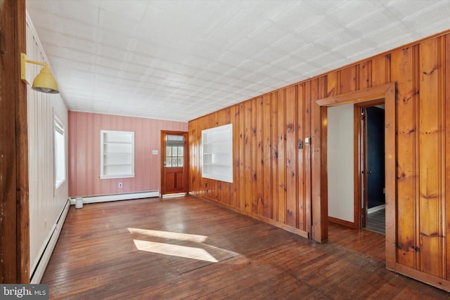 spare room featuring built in shelves, dark wood-type flooring, and a baseboard radiator