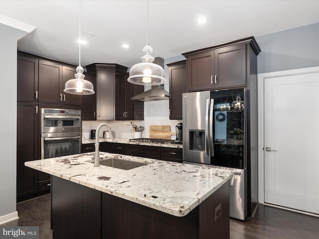 kitchen featuring hanging light fixtures, dark wood-type flooring, stainless steel appliances, and a center island with sink