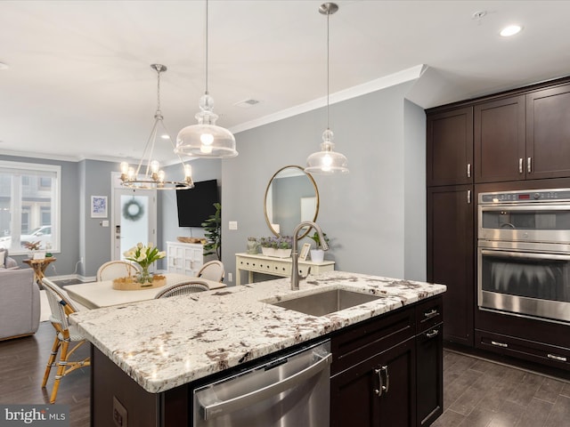 kitchen featuring appliances with stainless steel finishes, a kitchen island with sink, sink, and hanging light fixtures