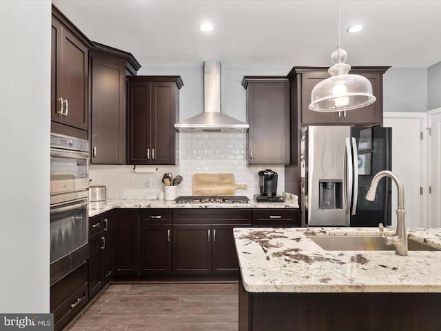 kitchen featuring sink, stainless steel appliances, tasteful backsplash, decorative light fixtures, and wall chimney exhaust hood