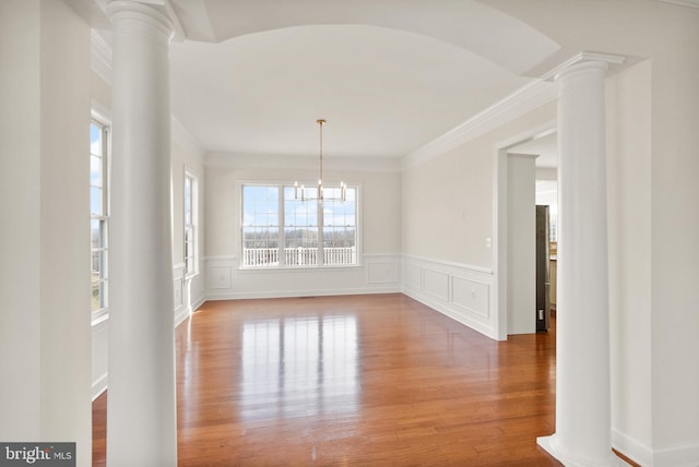 unfurnished dining area featuring decorative columns, wood-type flooring, an inviting chandelier, and crown molding