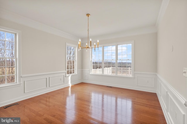 unfurnished dining area with an inviting chandelier, hardwood / wood-style floors, and crown molding