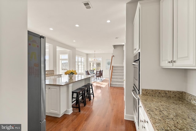 kitchen with stainless steel fridge, white cabinetry, hardwood / wood-style floors, light stone counters, and a kitchen bar