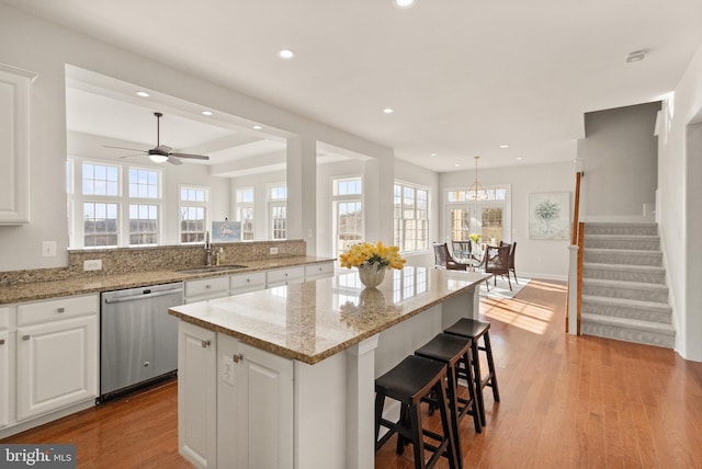 kitchen featuring white cabinetry, sink, a center island, stainless steel dishwasher, and light wood-type flooring