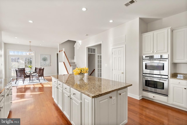 kitchen with white cabinetry, a center island, double oven, and light wood-type flooring