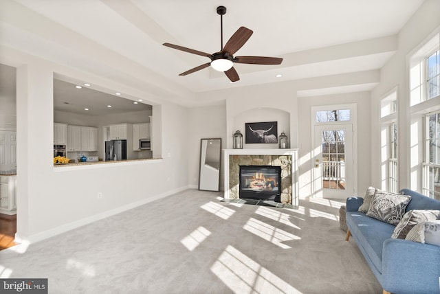 carpeted living room featuring a tray ceiling, a tile fireplace, and ceiling fan