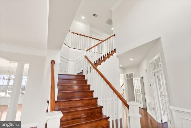 stairway featuring hardwood / wood-style floors, ornamental molding, decorative columns, and a high ceiling