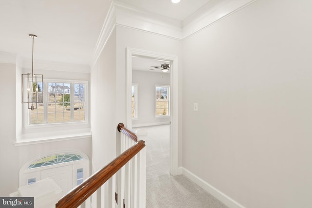 hall with ornamental molding, light colored carpet, and an inviting chandelier