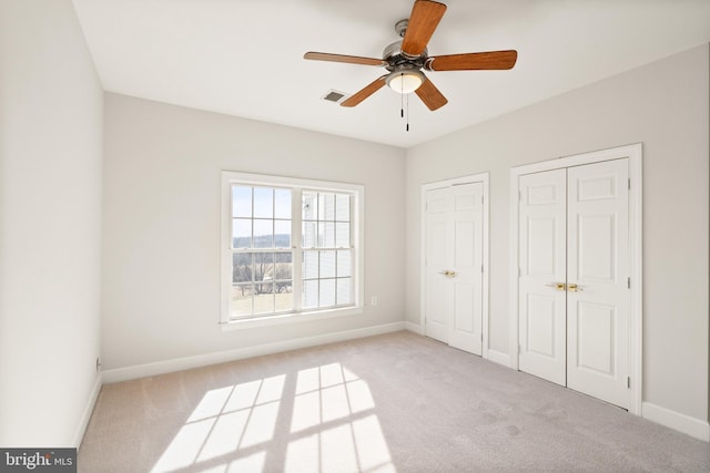 unfurnished bedroom with ceiling fan, light colored carpet, and two closets