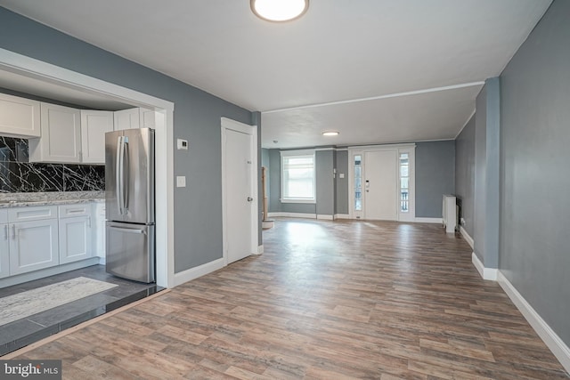 interior space featuring backsplash, dark wood-type flooring, light stone counters, white cabinetry, and stainless steel refrigerator