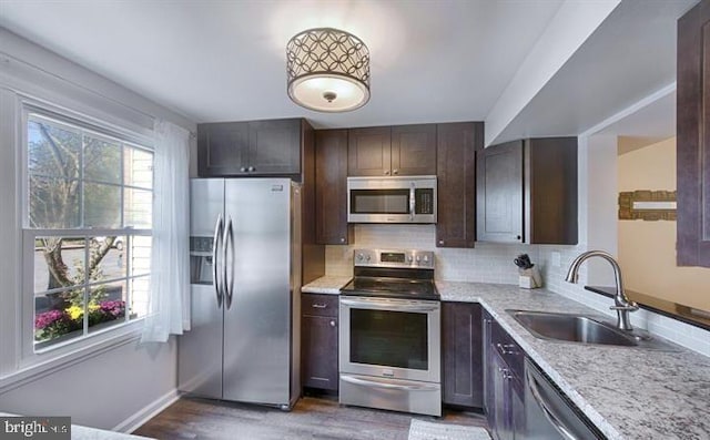 kitchen featuring appliances with stainless steel finishes, sink, dark hardwood / wood-style floors, light stone counters, and dark brown cabinets