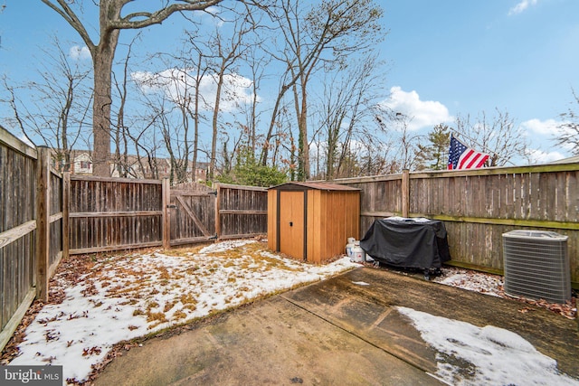 snow covered patio featuring central AC, a storage shed, and area for grilling