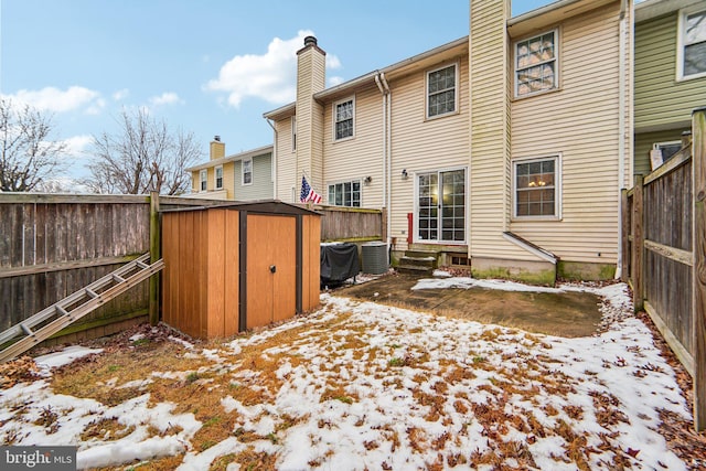 snow covered house featuring central AC unit and a shed