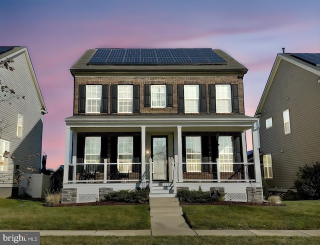 view of front of home with roof mounted solar panels, brick siding, covered porch, and a front yard