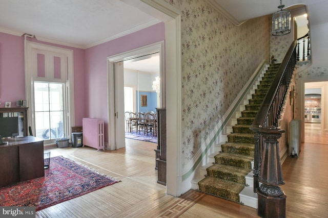 staircase featuring radiator heating unit, an inviting chandelier, crown molding, and wood-type flooring