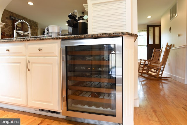 bar featuring white cabinetry, sink, beverage cooler, light hardwood / wood-style flooring, and dark stone countertops