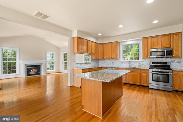 kitchen featuring visible vents, a kitchen island, open floor plan, light stone countertops, and stainless steel appliances