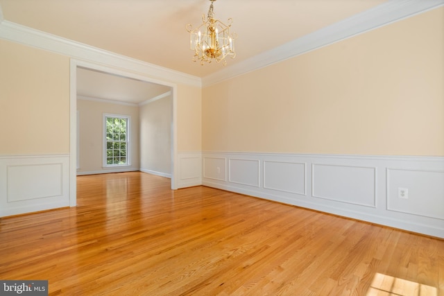 unfurnished room with ornamental molding, light wood-type flooring, wainscoting, and an inviting chandelier