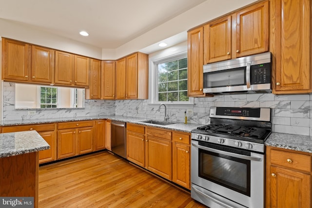 kitchen featuring light wood-style flooring, light stone countertops, stainless steel appliances, a sink, and brown cabinets