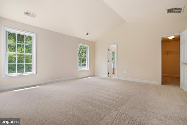 empty room featuring baseboards, visible vents, vaulted ceiling, and light colored carpet