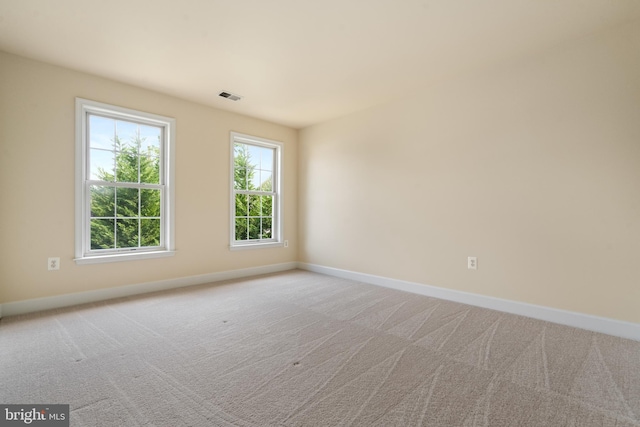 spare room featuring light colored carpet, visible vents, and baseboards