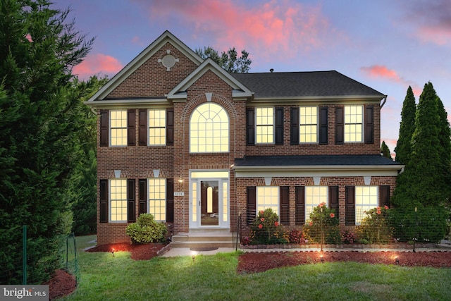 view of front of property with roof with shingles, a front lawn, and brick siding