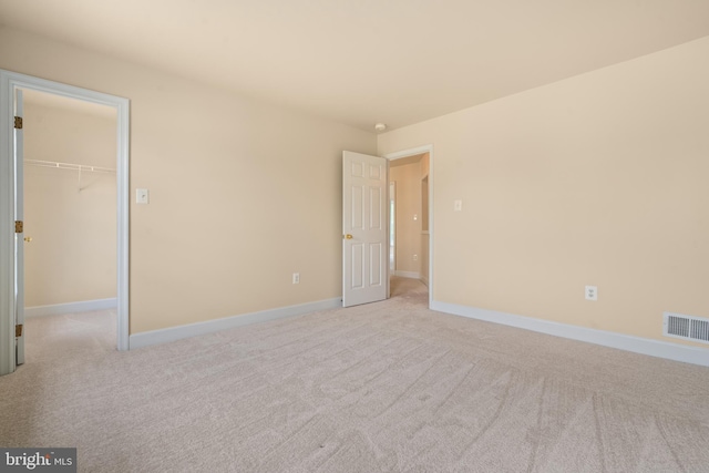 unfurnished bedroom with a closet, visible vents, a spacious closet, light carpet, and baseboards