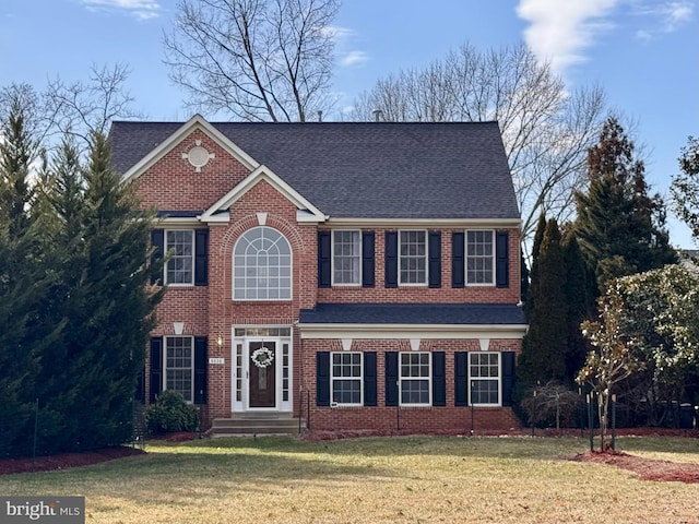 view of front facade with brick siding, roof with shingles, and a front yard