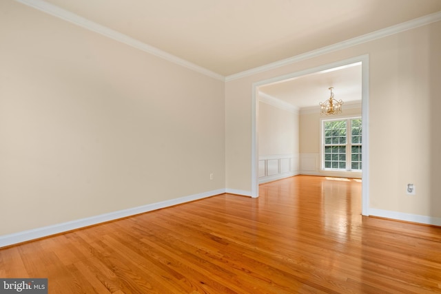 unfurnished room featuring light wood finished floors, a wainscoted wall, ornamental molding, a decorative wall, and a notable chandelier