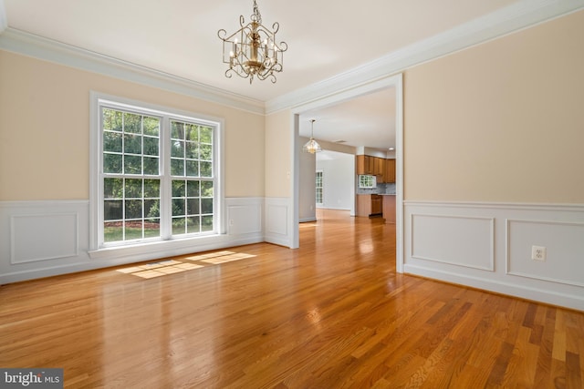 unfurnished dining area with light wood finished floors, ornamental molding, a notable chandelier, and wainscoting