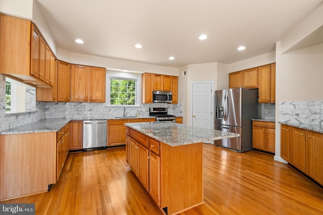 kitchen with light stone counters, light wood-style flooring, appliances with stainless steel finishes, a kitchen island, and a sink