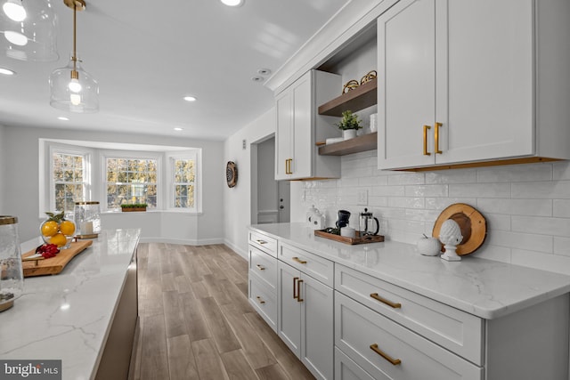 kitchen featuring tasteful backsplash, light wood-type flooring, light stone counters, and decorative light fixtures